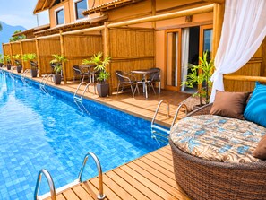 A poolside area with a wooden deck, lounge chairs, and a small table. - Tahaa Pousada Boutique (Ilhabela)