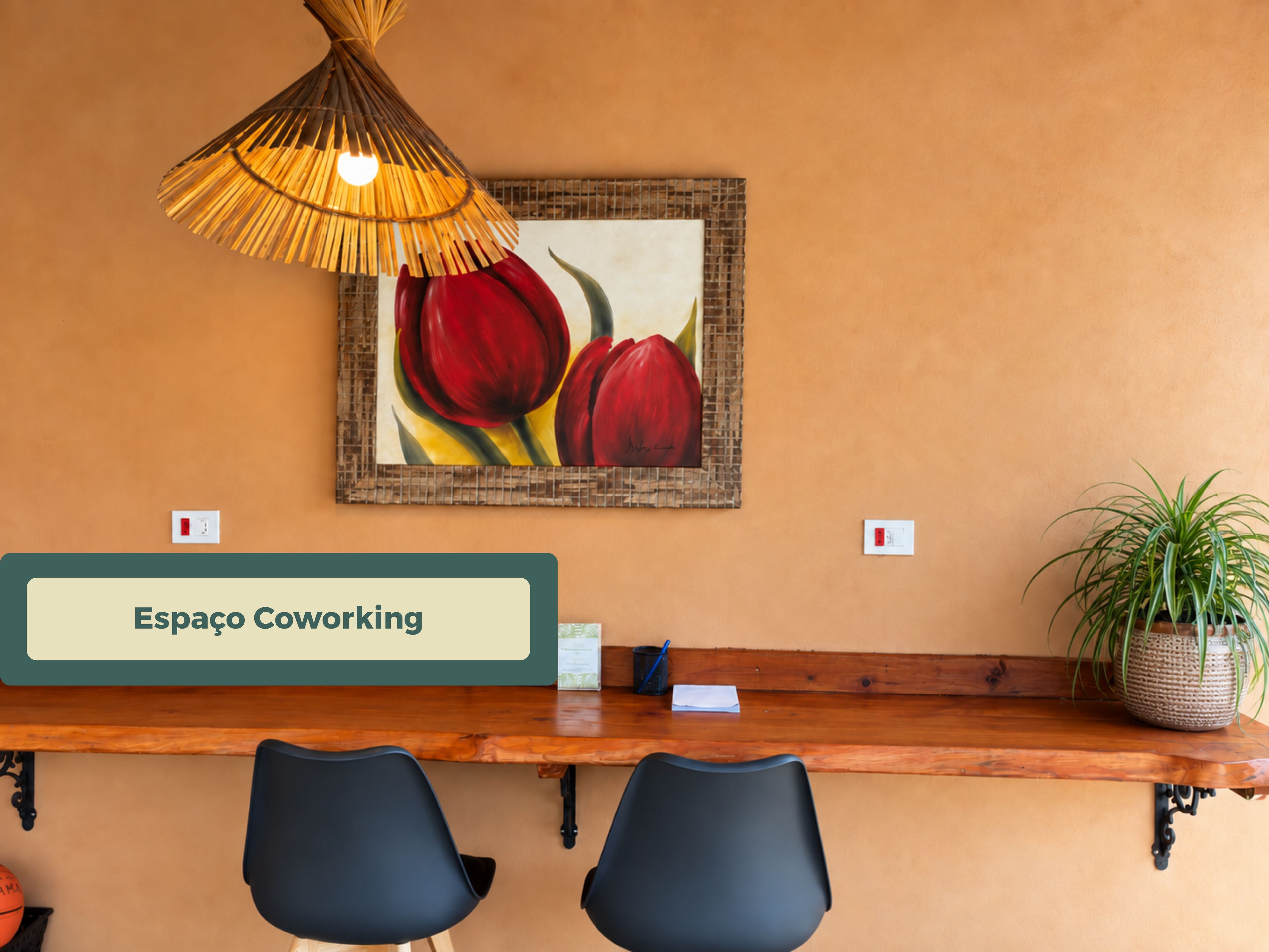 Un espacio de coworking con un escritorio de madera, dos sillas negras, una lámpara colgante y un cuadro enmarcado con tulipanes rojos en la pared.