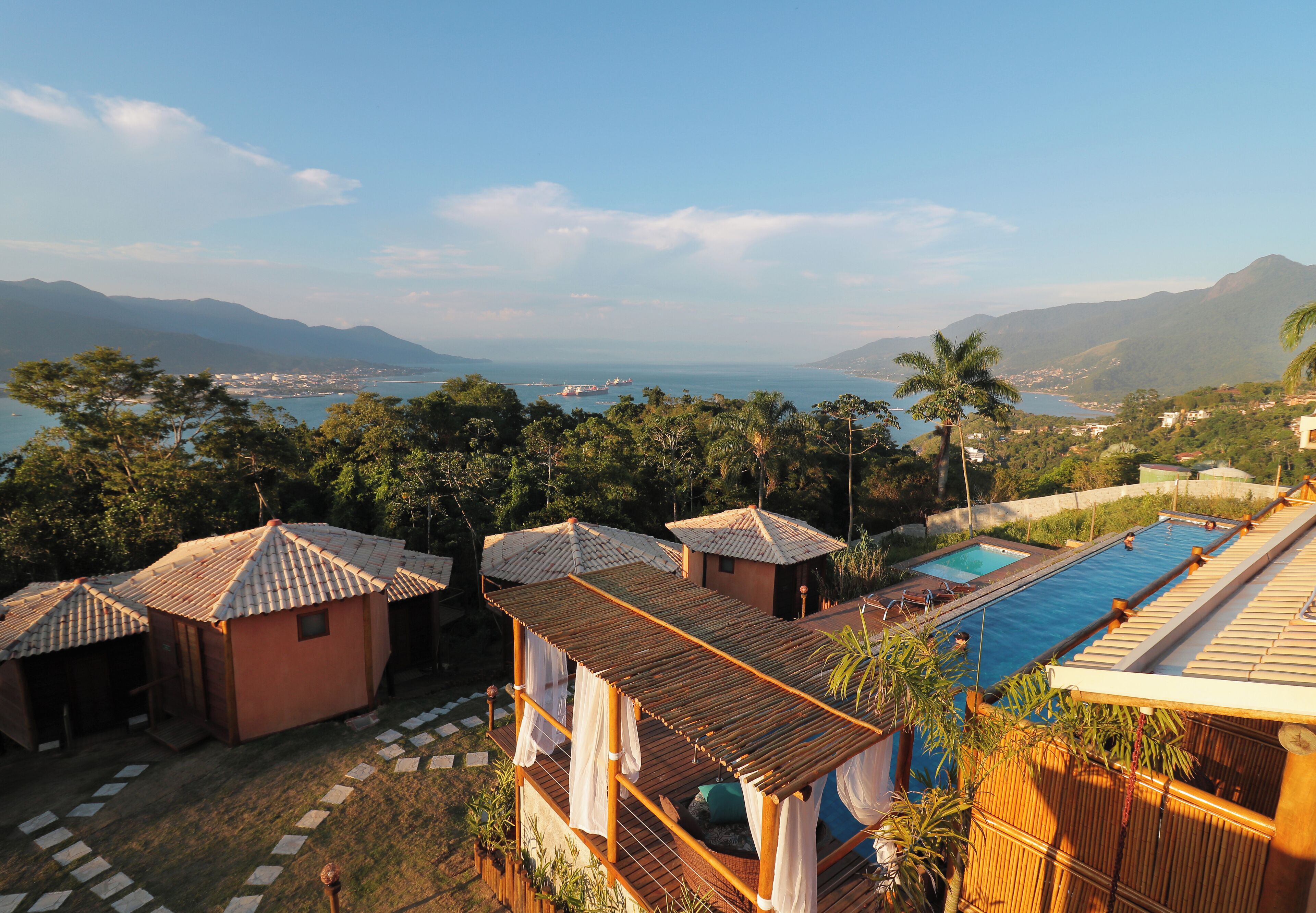 Un resort con varias cabañas, una piscina y vistas al mar y a las montañas.