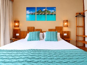 A hotel room with a large bed, two nightstands, a wooden headboard, a teal knitted throw, and a wall with a tropical landscape painting. - Tahaa Pousada Boutique (Ilhabela)