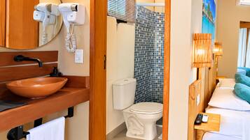 Un baño con tocador de madera, lavamanos, inodoro y zona de ducha.