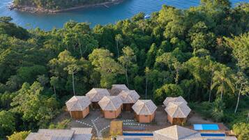 Un complex turístic amb diverses allotjaments tipo bungalow, una piscina i una vista d'una illa tropical.