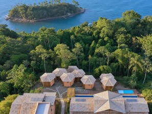 Un resort con diverse sistemazioni in stile bungalow, una piscina e vista su un'isola tropicale.