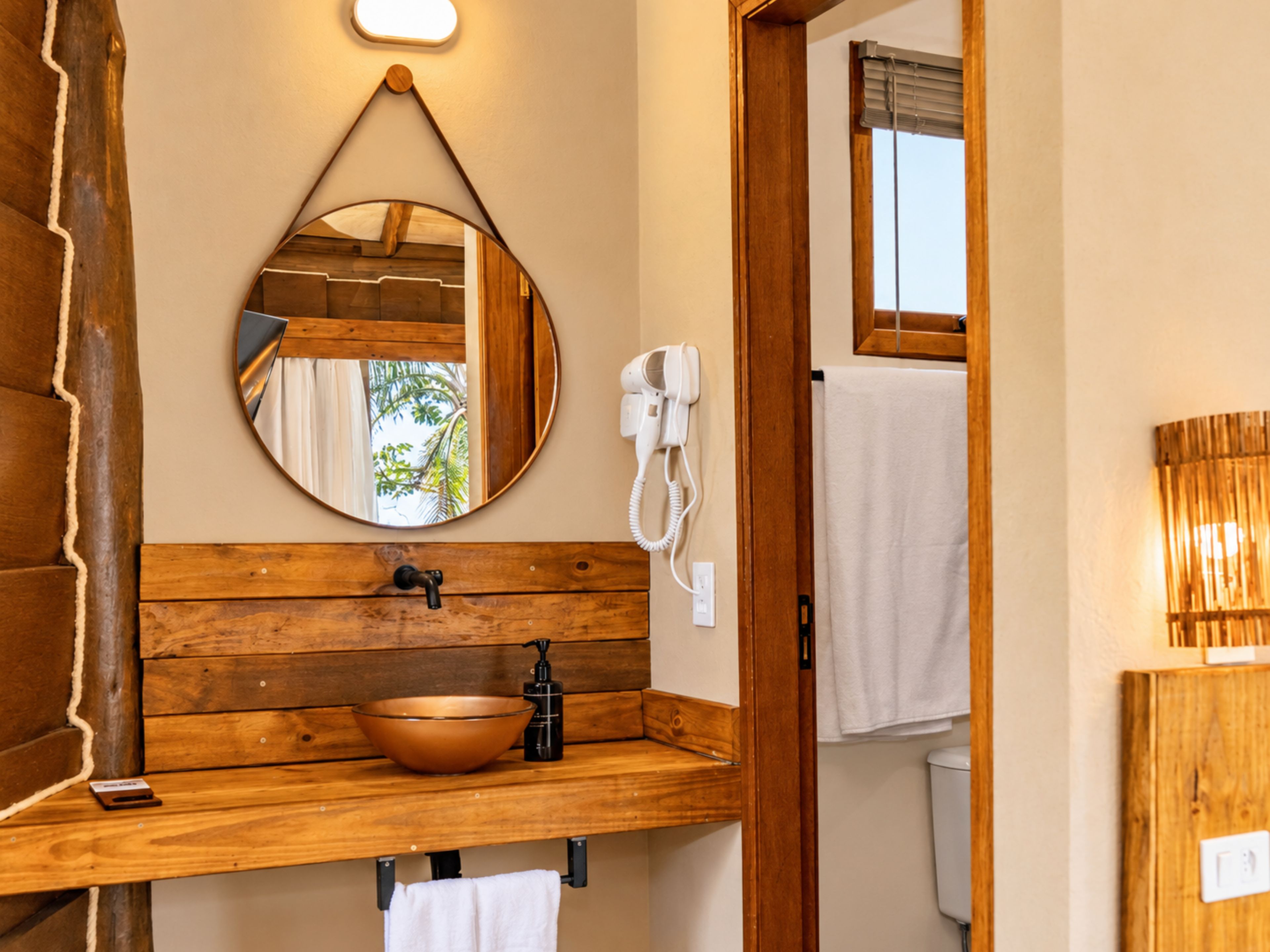 A bathroom with a wooden vanity, a round mirror, a sink with a bowl, a handheld showerhead, and a white towel hanging on a rack.