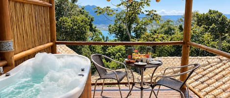 A wooden deck with a hot tub, two chairs, and a table with breakfast items.