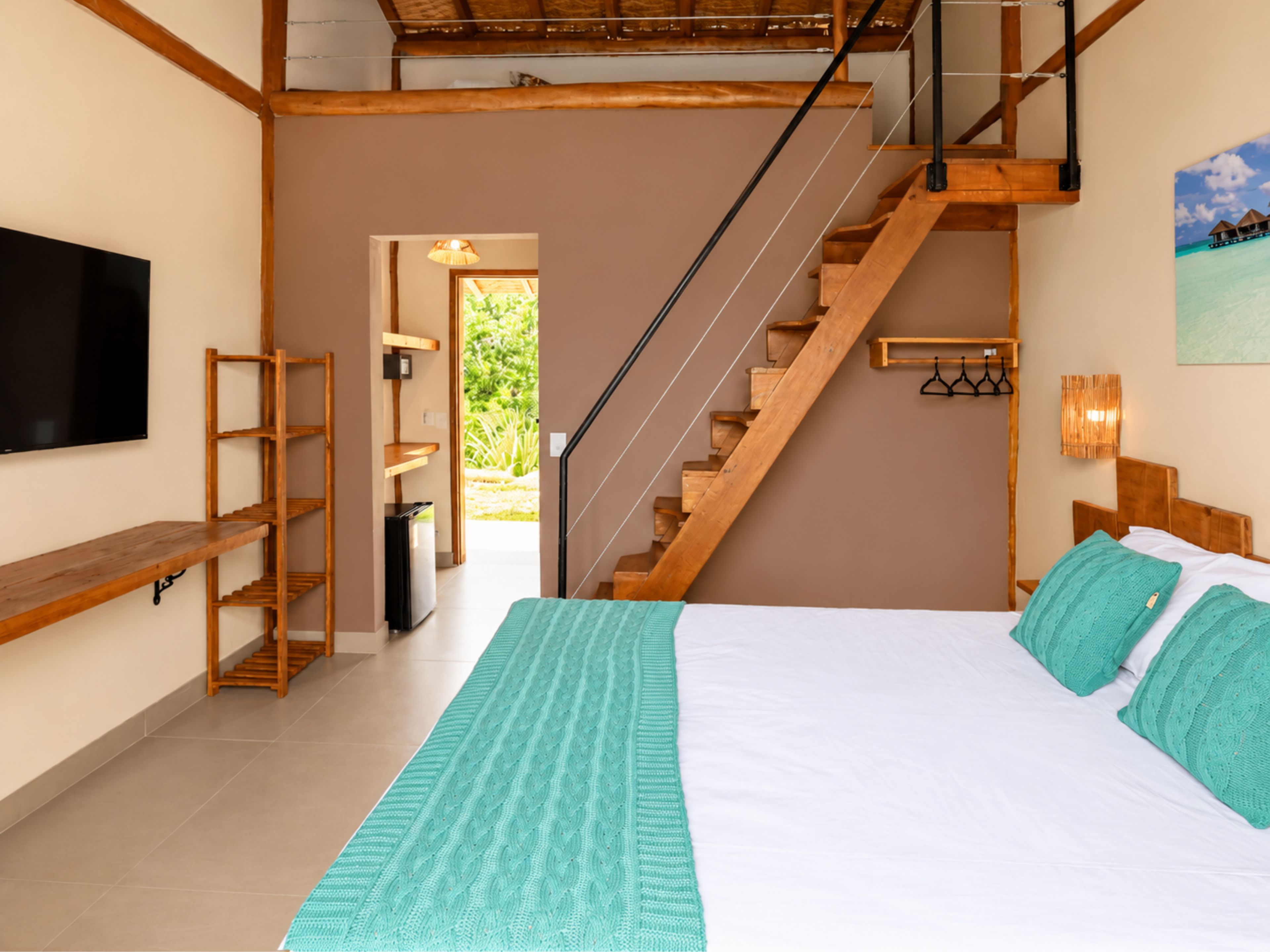 A bedroom with a bed, a wooden staircase, a TV, and a view of the outdoors.