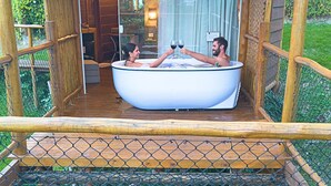 A wooden deck with a glass-enclosed hot tub where two people are toasting with wine glasses. - Tahaa Pousada Boutique (Ilhabela)