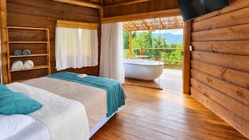 Habitació d'una cabana de fusta amb un llit, una estant amb tovalloles, una banyera i un televisor fixat a la paret.