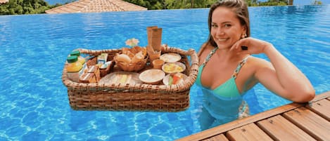 A person in a pool with a floating basket containing food and drinks.
