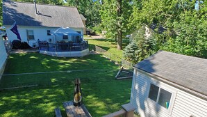 Un jardin à l’arrière d’une maison, comprenant une terrasse couverte, une plateforme en bois et un petit abri de jardin.