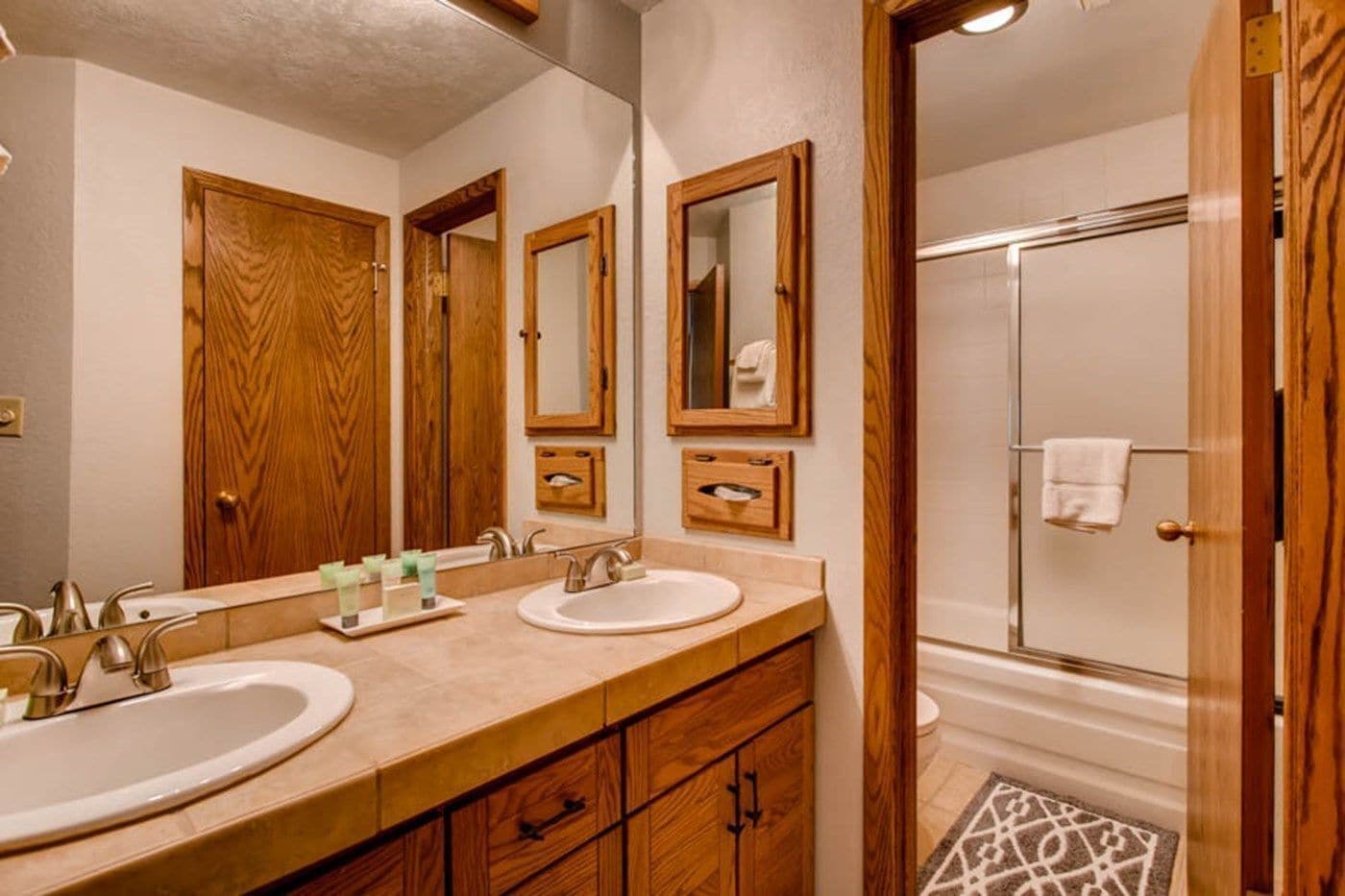 A bathroom with two sinks, wooden cabinets, a large mirror, and a shower area.