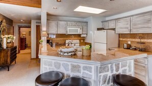 A modern kitchen with a central island, stone accents, and a stone wall. - Condo | 100 Yards from the Slopes | Cozy + Elegant (Crested Butte)