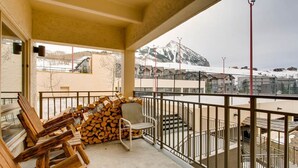 A balcony with stacked firewood, a chair, and a view of a snowy mountain. - Condo | 100 Yards from the Slopes | Cozy + Elegant (Crested Butte)