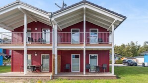 Un bâtiment à deux étages doté de balcons, d’un espace extérieur couvert aménagé en coin salon et d’une voiture garée à proximité.