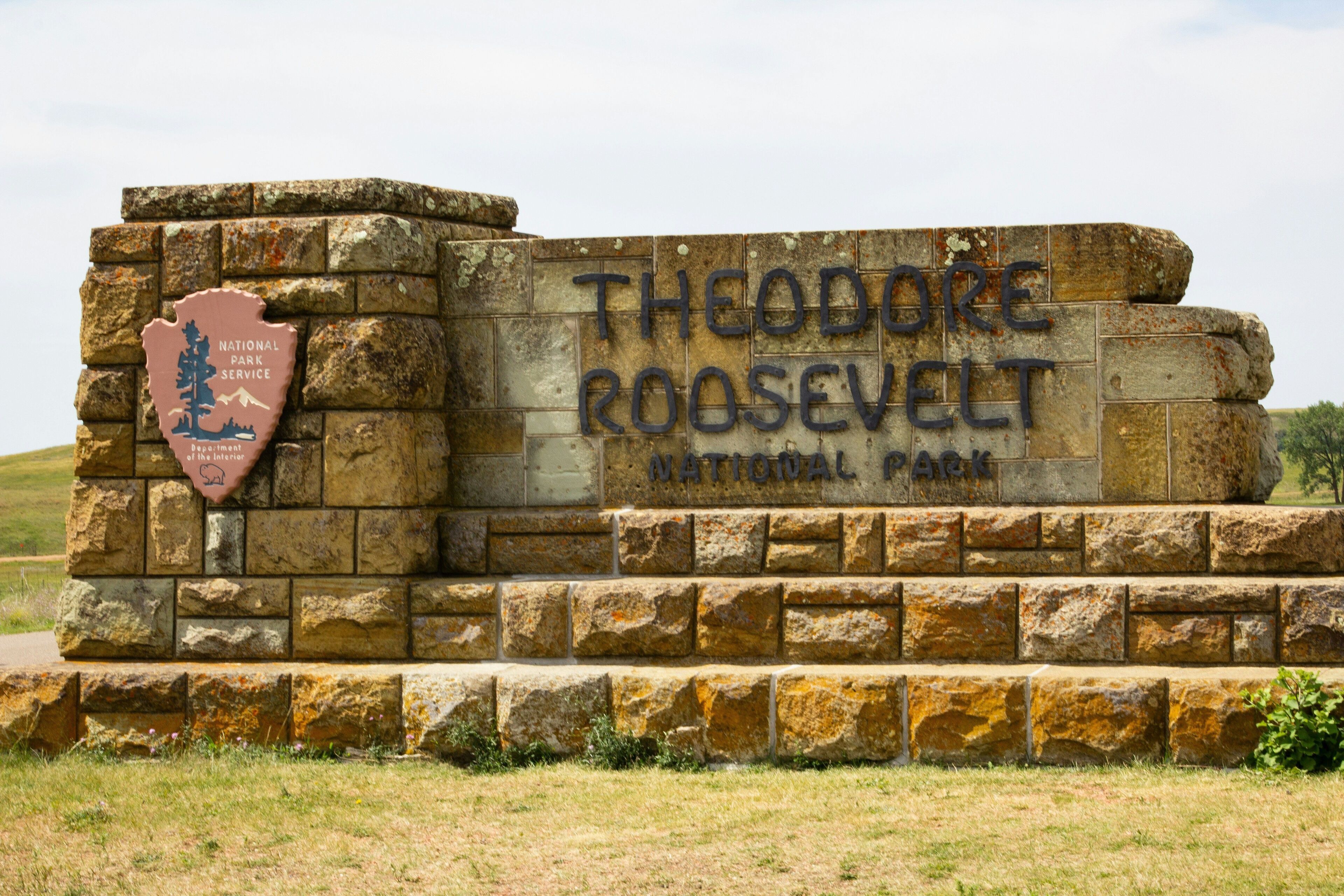 Un letrero de piedra con la leyenda "Theodore Roosevelt National Park" y el emblema del Servicio de Parques Nacionales.
