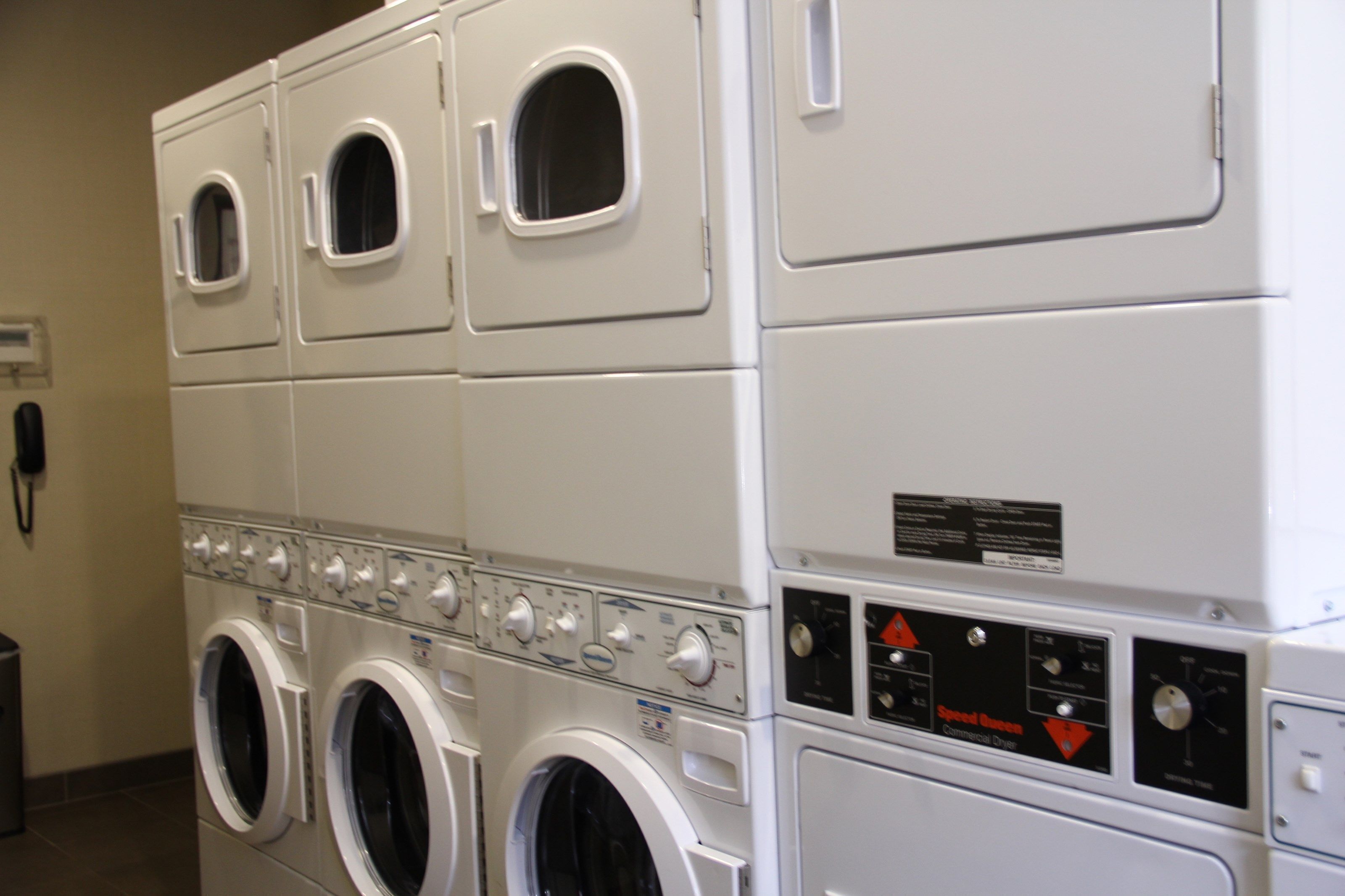 A laundry facility with multiple washing machines and dryers, control panels, and a telephone.
