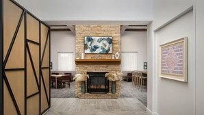 A room with a fireplace, wooden herringbone flooring, a dining area, and a framed abstract painting on the wall.