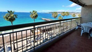 A balcony with a view of the sea, palm trees, and a distant cityscape.