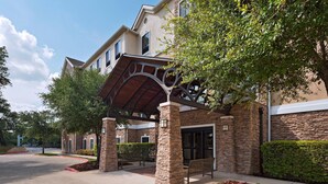 A building with a covered entrance, stone pillars, and a bench.
