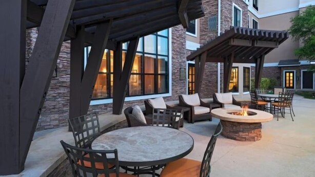 An outdoor patio with round tables and chairs, a stone fire pit, and a covered seating area.