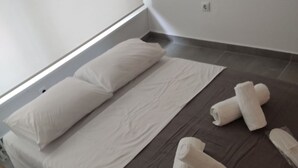 A neatly made bed with white linens and a brown throw blanket, accompanied by rolled white towels on the floor. - Studio Stratos With 1 Bathrooms (Athens)