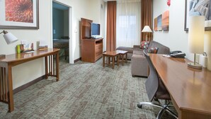 A hotel room with a wooden desk, a sofa, a television, and a bed.