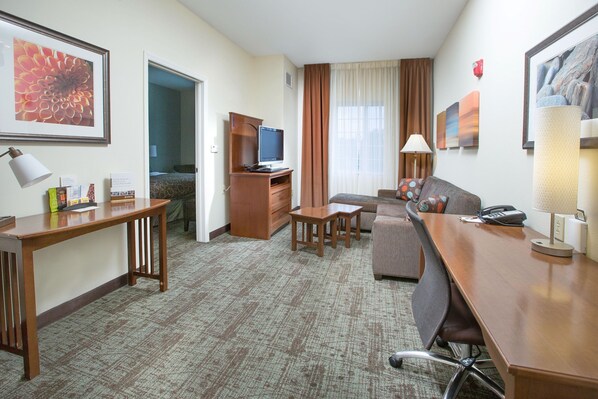 A hotel room with a wooden desk, a sofa, a television, and a bed.