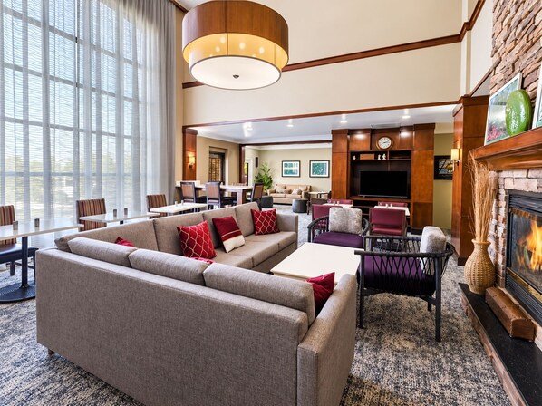 Un hall de hotel con un sofá grande, comedor, televisor, chimenea y ventanas amplias.