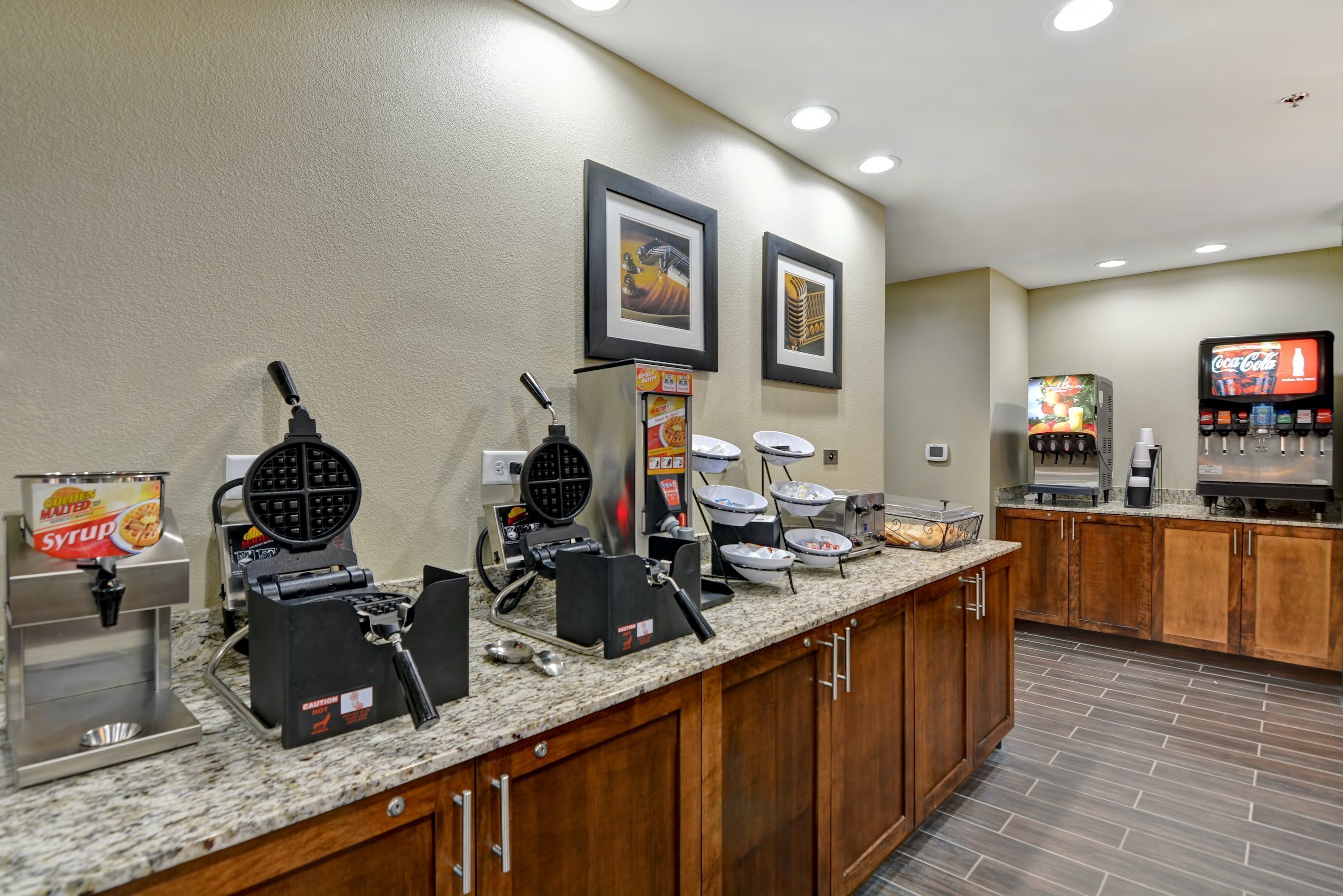 A breakfast bar with waffle makers, a Coca-Cola dispenser, and a coffee machine.