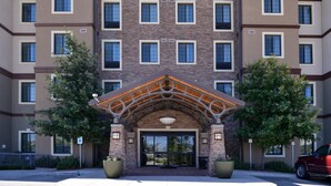 A multi-story building with a central entrance featuring a wooden archway and large potted plants on either side.
