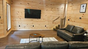 Ein Holzinnenraum mit einer Ledersofa, einem Couchtisch und einem an der Wand befestigten Flachbildfernseher.