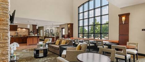 Un hall de hotel espacioso con un comedor, una cocina al fondo y grandes ventanales que ofrecen una vista.