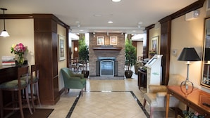 A hotel lobby with a fireplace, seating area, and reception desk. - 1BR Condo | Free Breakfast + Indoor Pool (Fort Wayne)
