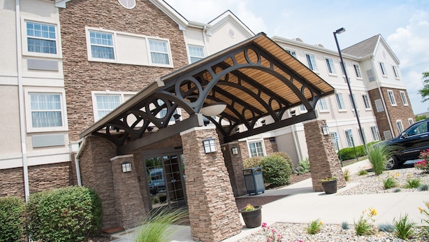 A building with a stone facade, a covered entrance, and a parking area with a car. - 1BR Condo | Free Breakfast + Indoor Pool (Fort Wayne)