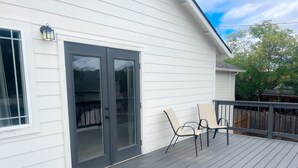 A deck with two chairs and a table, a sliding glass door, and a lantern on the wall. - Elevated Eugene Retreat: Bright, Calm & Spacious (Eugene)