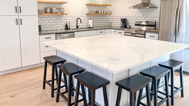 A modern kitchen with white cabinets, a large island with bar stools, a stainless steel range hood, and a built-in oven. - Elevated Eugene Retreat: Bright, Calm & Spacious (Eugene)