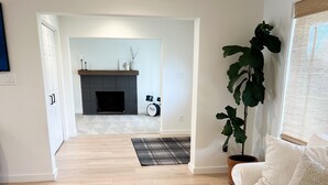 A living room with a wooden coffee table, a white sofa, a large potted plant, and a fireplace in the background. - Elevated Eugene Retreat: Bright, Calm & Spacious (Eugene)