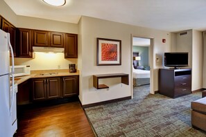 Une chambre d’hôtel compacte, dotée d’une kitchenette, d’un téléviseur à écran plat et d’une œuvre d’art encadrée au mur.