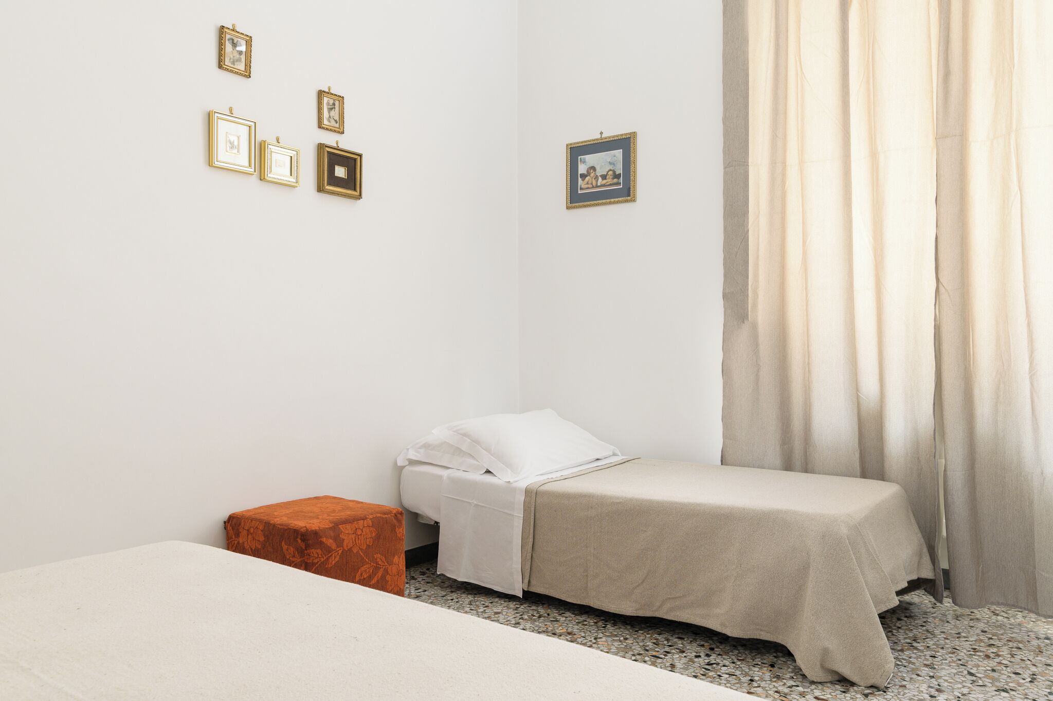 A small, neatly arranged bedroom with a single bed, a small table, and a few framed pictures on the wall.