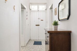 Een hal met een witte deur, een plantje op een houten toonbank en een spiegel aan de muur.