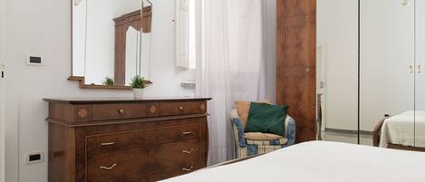 Un dormitorio con un aparador de madera, una cama, un espejo y una ventana con cortinas.
