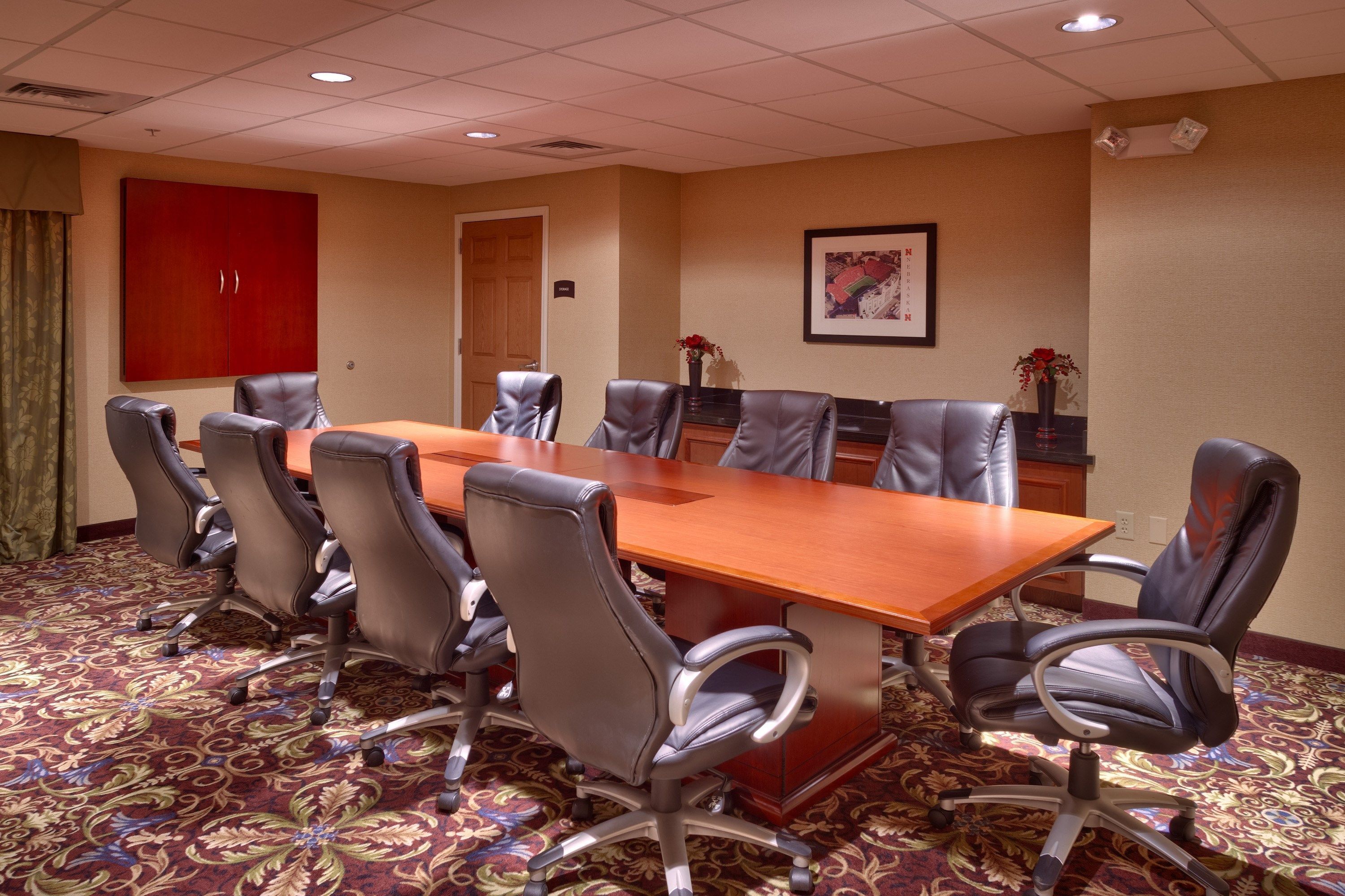 A conference room with a large table, six chairs, a red cabinet, and a framed picture on the wall.