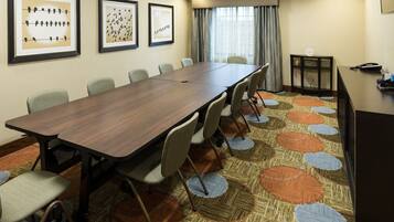 A conference room with a long table, chairs, framed artwork on the wall, and a carpeted floor.