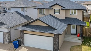 A residential house with a garage, a stone accent wall, and a well-maintained lawn. - Spacious 4BR-4BA House for Large Families & Group in Stonebridge (Saskatoon)
