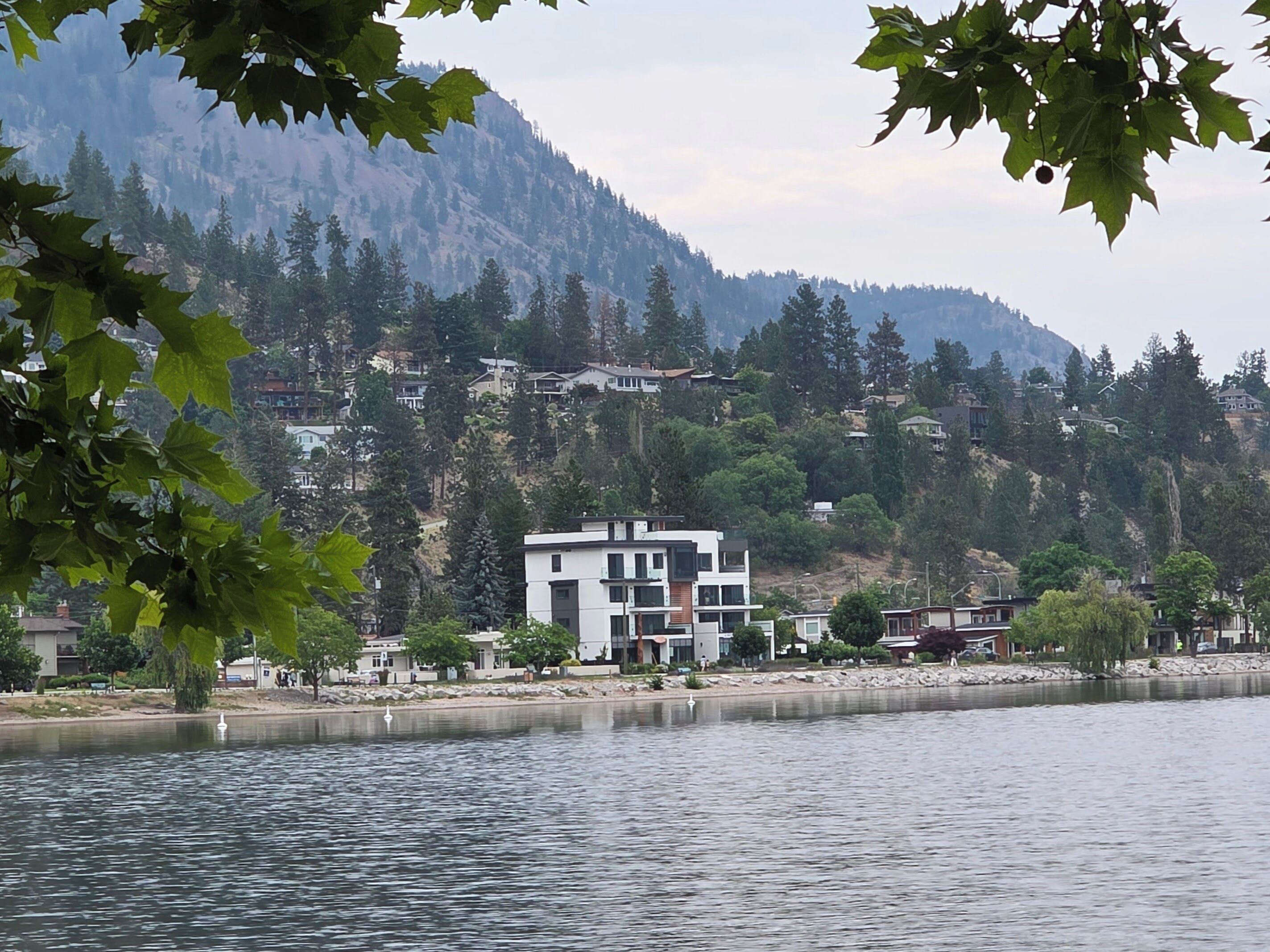 A modern building with a flat roof, located near a body of water with a mountain backdrop.