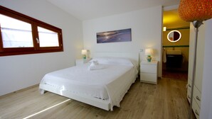 Ein Schlafzimmer mit einem Bett, zwei Nachttischen, einem Fenster, einem Gemälde, einem Spiegel und einer Lampe.
