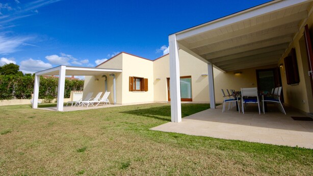 Ein modernes Haus mit überdachter Terrasse, Rasenfläche und Schwimmbecken.