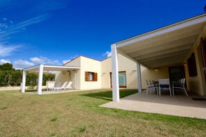 A modern house with a covered patio area, a lawn, and a pool.