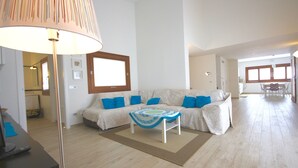 Ein Wohnzimmer mit Sofa, Couchtisch und Lampe. Im Hintergrund sind ein Fenster und eine Tür zu sehen.