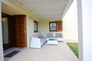 A covered patio with a white sofa, wooden shutters, and a glass door.